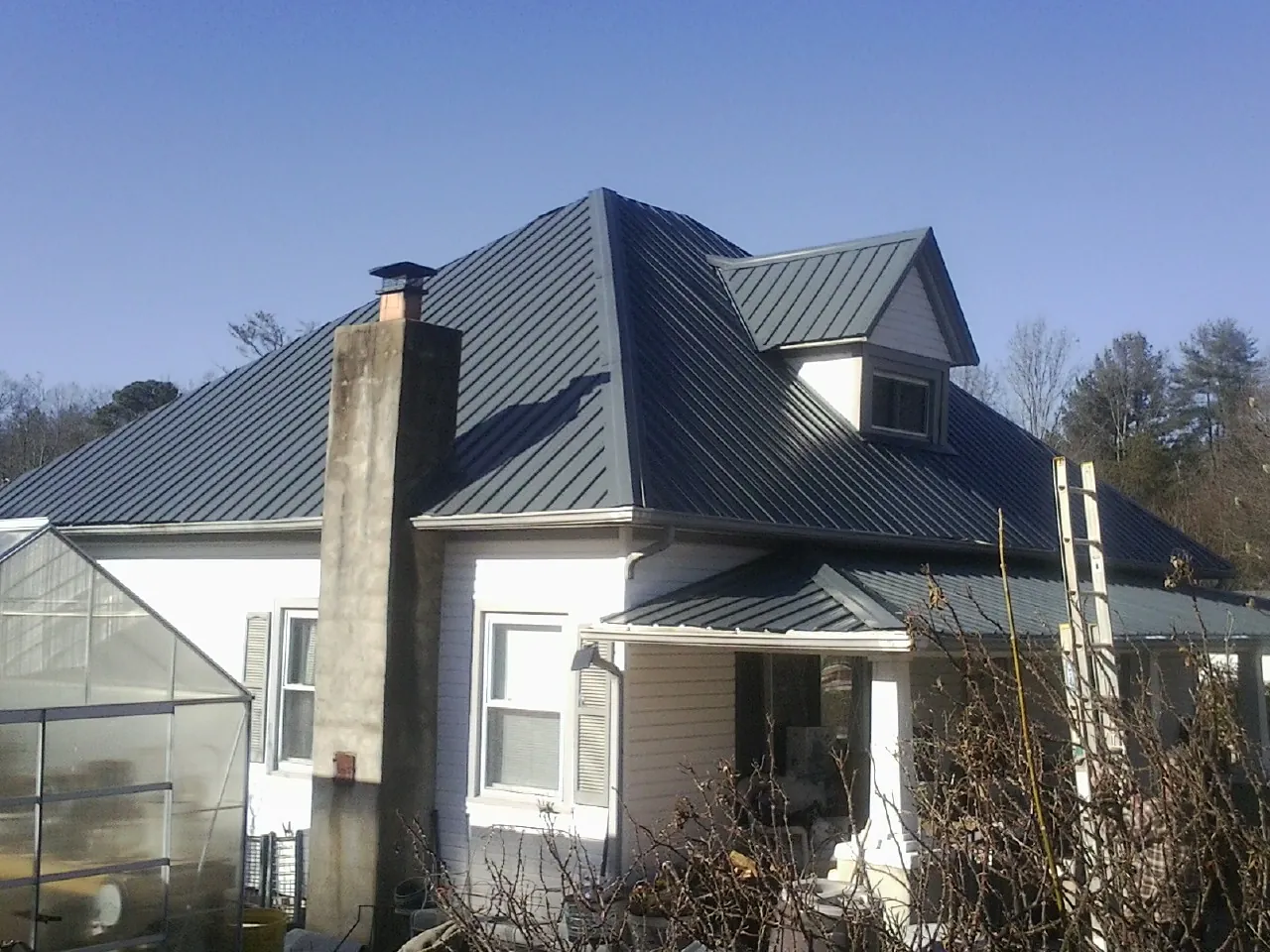 Dark blue standing seam metal roof on a white farmhouse with dormer — Slate & Tile Roof Repair by Roofing Brothers in Saddle Brook
