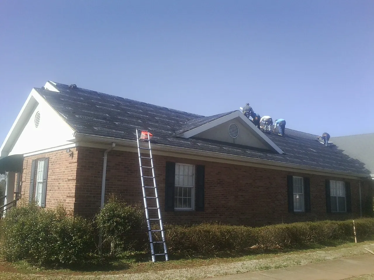 Crew tearing shingles off a brick ranch roof with a ladder set — Emergency Roof Repair work by our crew in Saddle Brook
