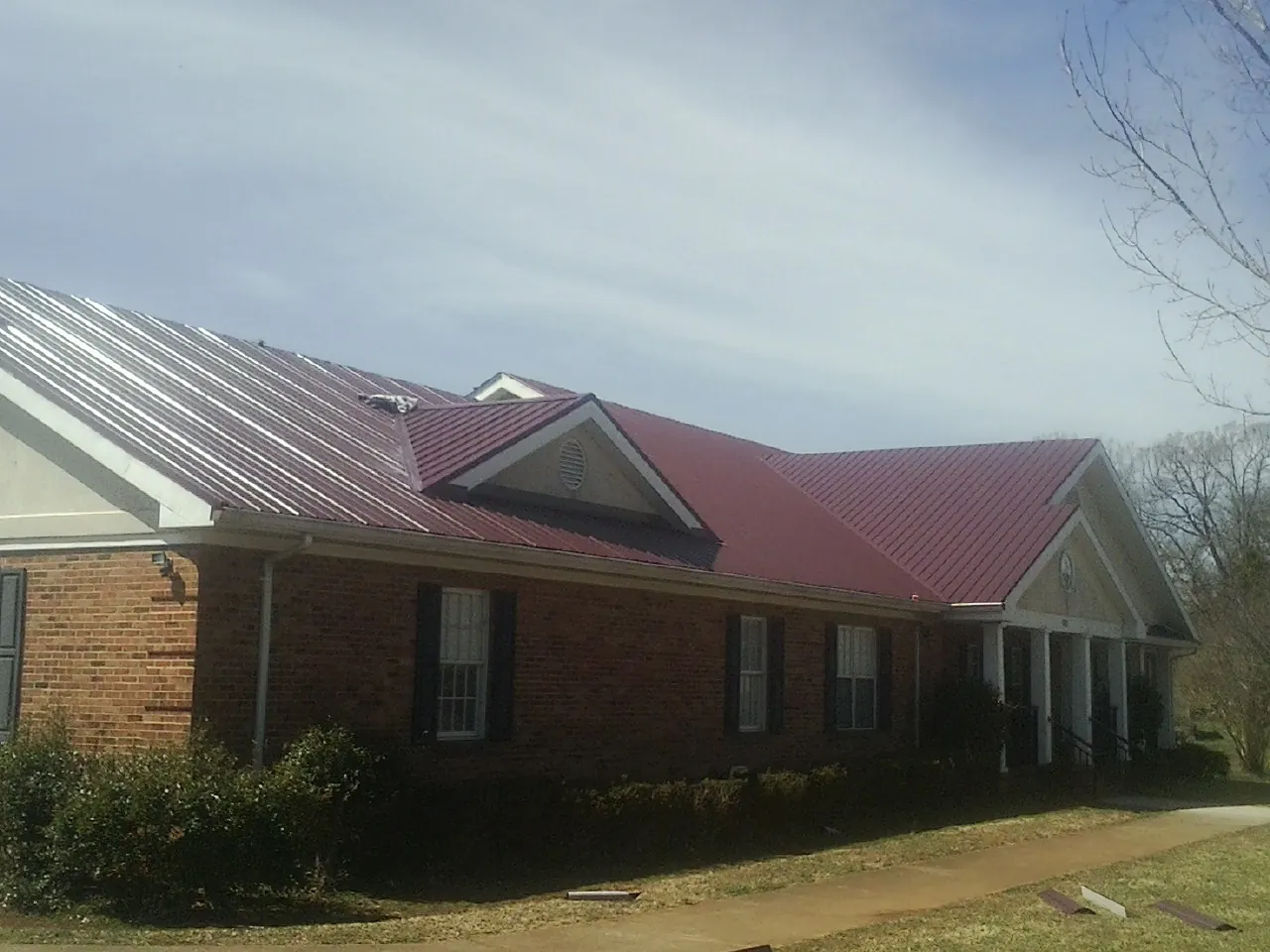 Red metal roof with gabled entries on a long brick building, from a Hail Damage Roof Repair job in Saddle Brook