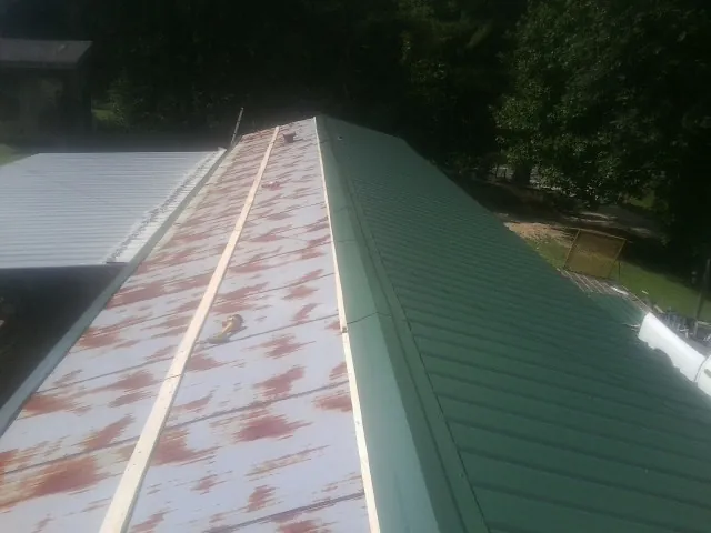 Old rusted panels beside newly installed green metal roofing — Wind Damage Roof Repair by Roofing Brothers in Saddle Brook