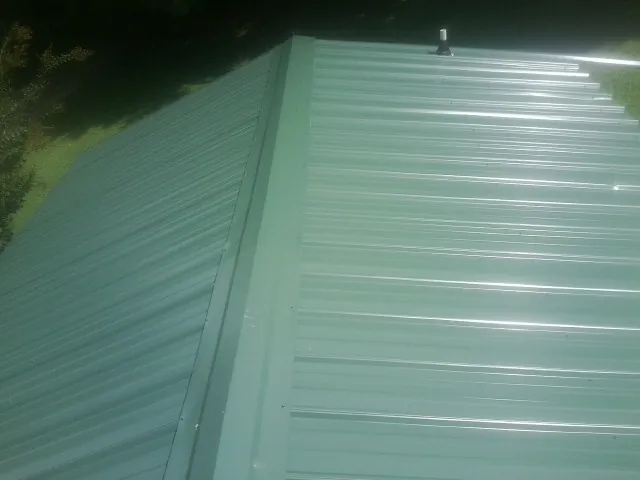 New green metal panels meeting at the ridge of a roof — Flat Roof Repair work by our crew in Saddle Brook