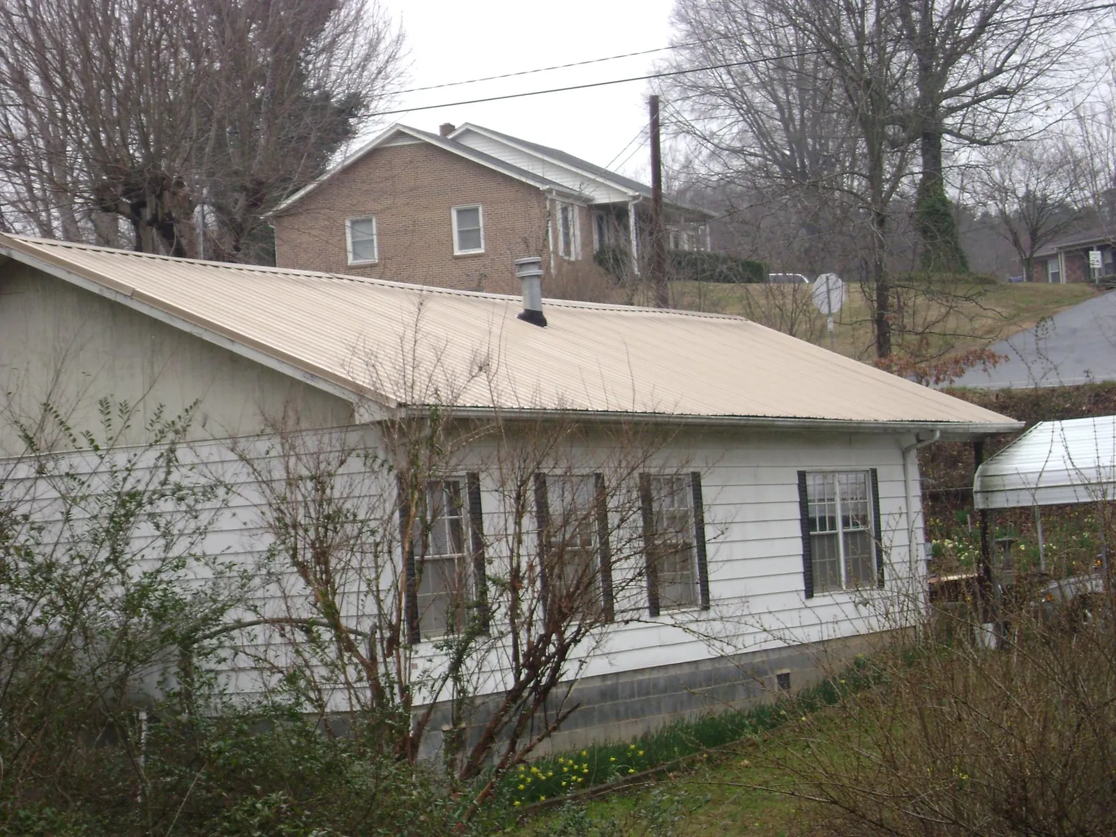 Tan metal roof on a white sided house set into a hillside — Commercial Roofing by Roofing Brothers in Saddle Brook